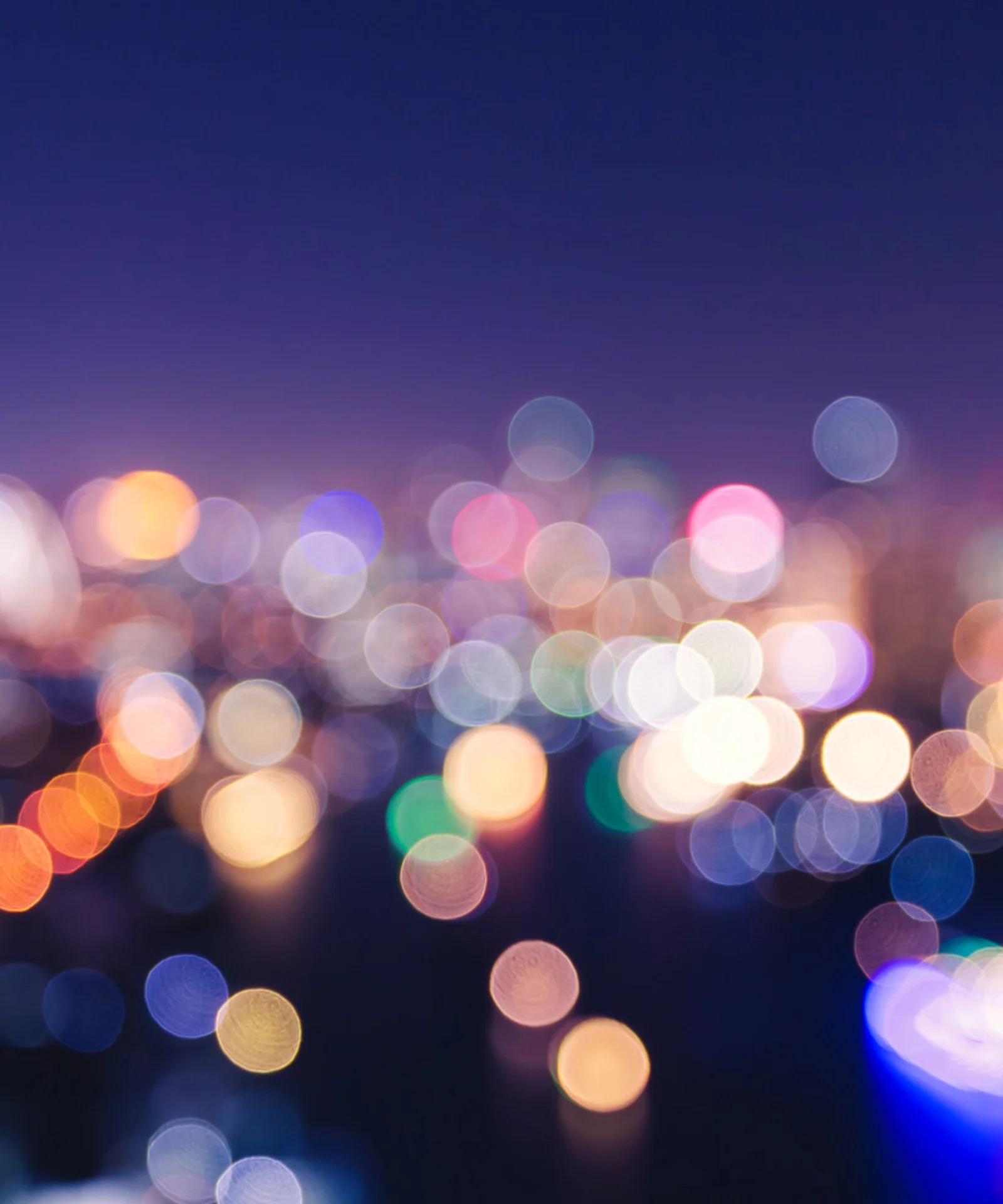 A blurred image of colorful city lights glowing against a dark night sky, creating a bokeh effect.