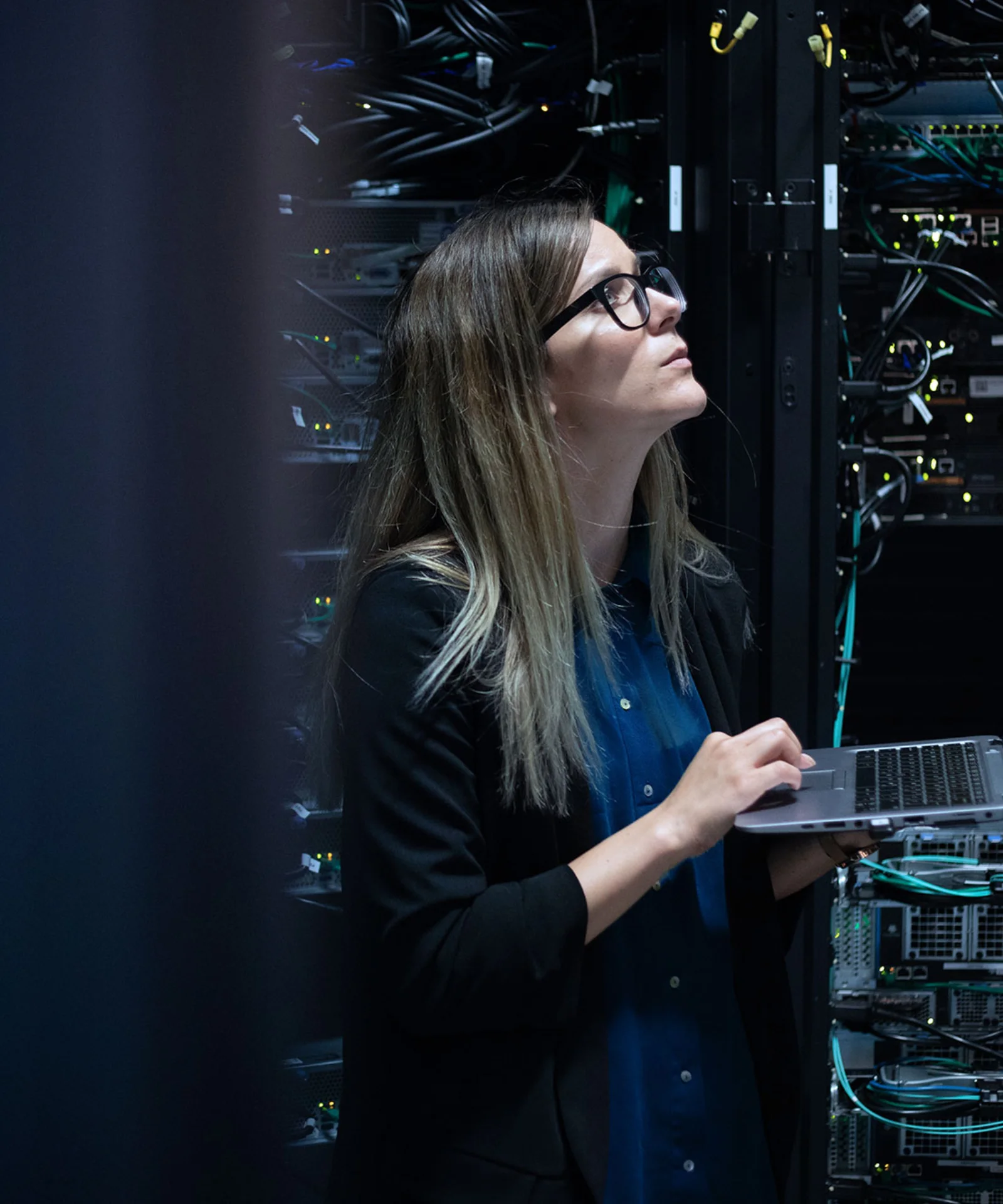 A female IT professional works on a laptop in a server room, surrounded by networking cables and server equipment, representing a high-performance computing (HPC) solution.