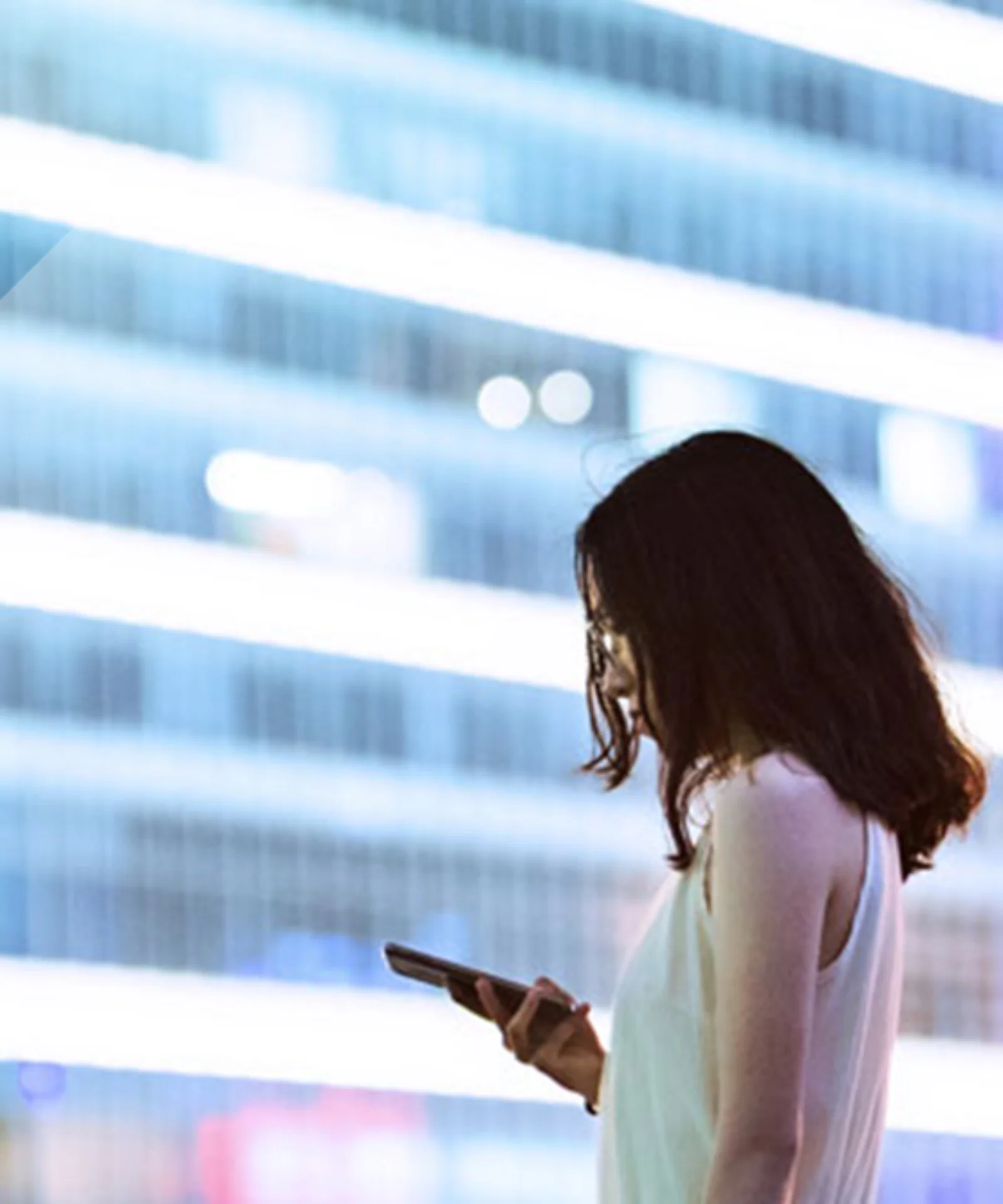 A professional woman using her smartphone with a modern cityscape in the background, symbolizing the impact of Central Bank Digital Currencies (CBDCs) on the future of commercial banking.