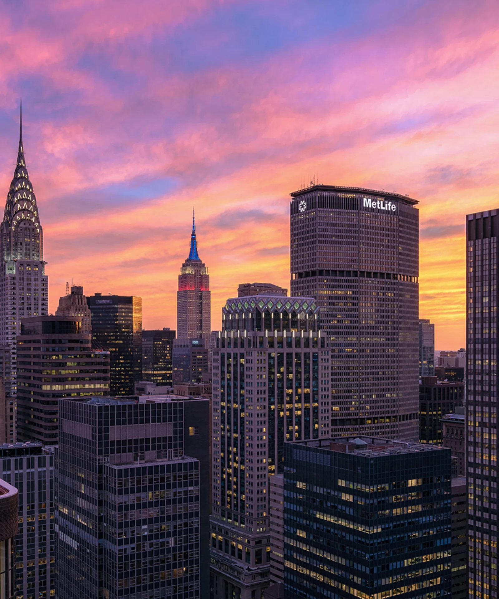 A vibrant sunset over the New York City skyline, featuring iconic skyscrapers such as the Chrysler Building and the MetLife Tower.