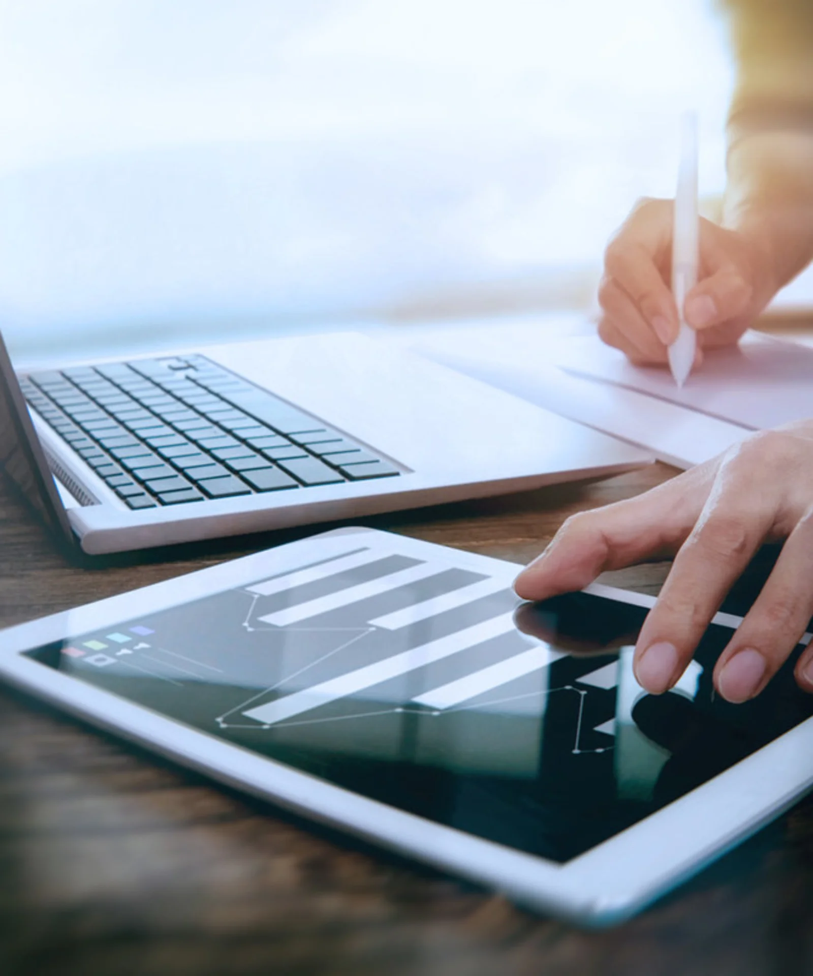 Close-up of a person working on a tablet with a laptop nearby, representing a modern digital work environment with multitasking and data analysis.