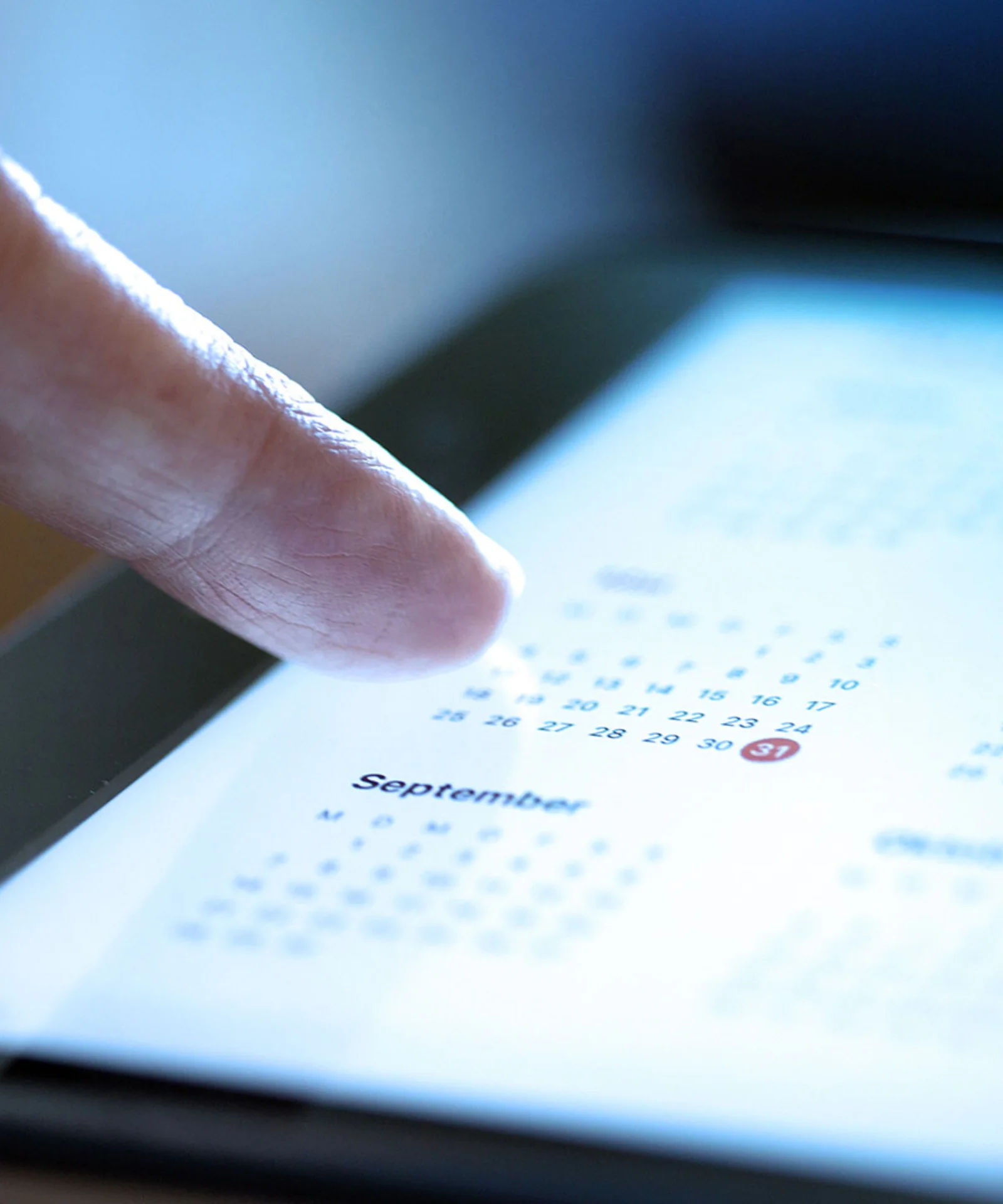 A close-up of a hand interacting with a digital calendar on a tablet, highlighting a date, symbolizing important financial and scheduling events.