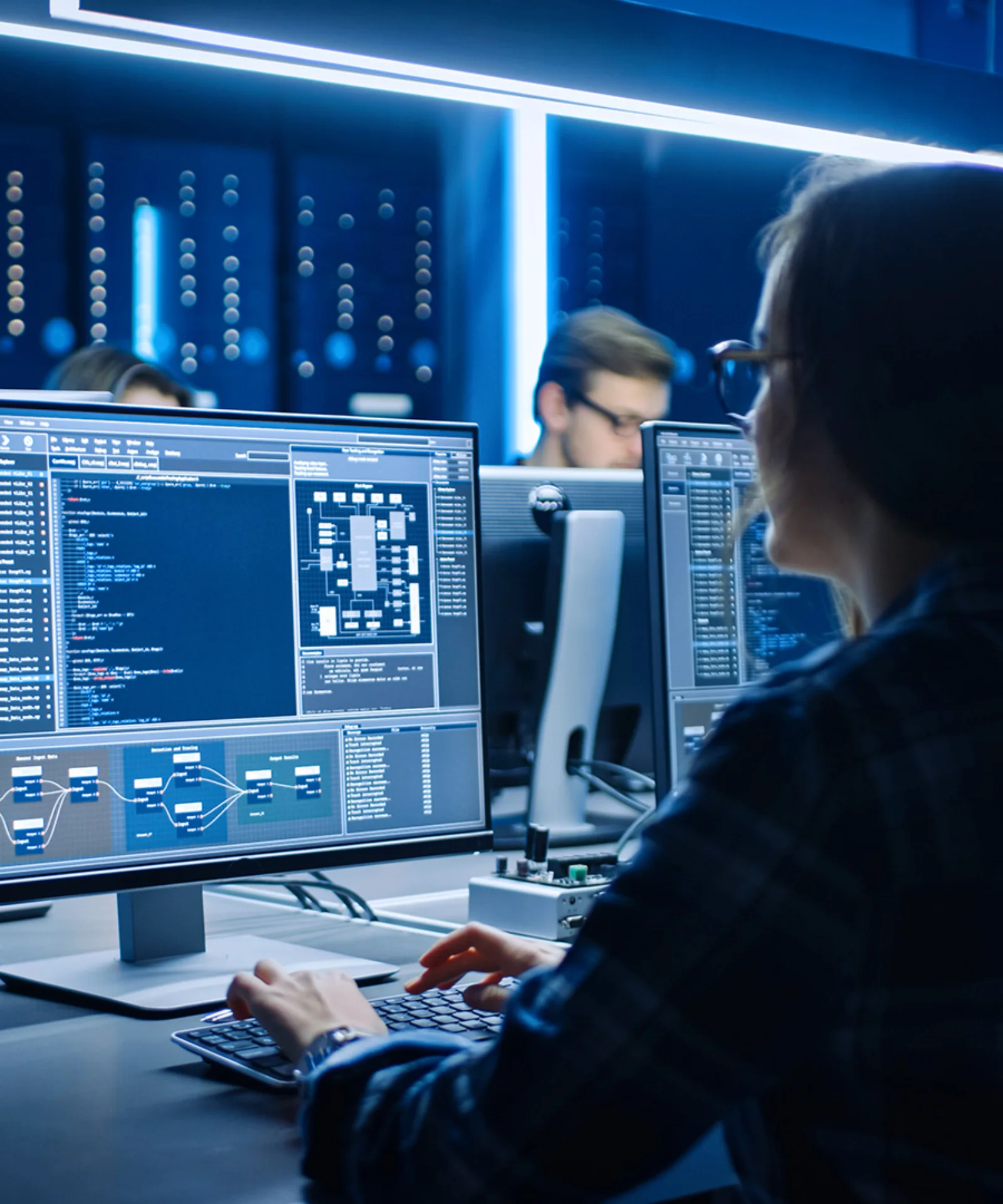 Software engineer working on multiple monitors displaying complex code and data visualisations in a high-tech office environment.