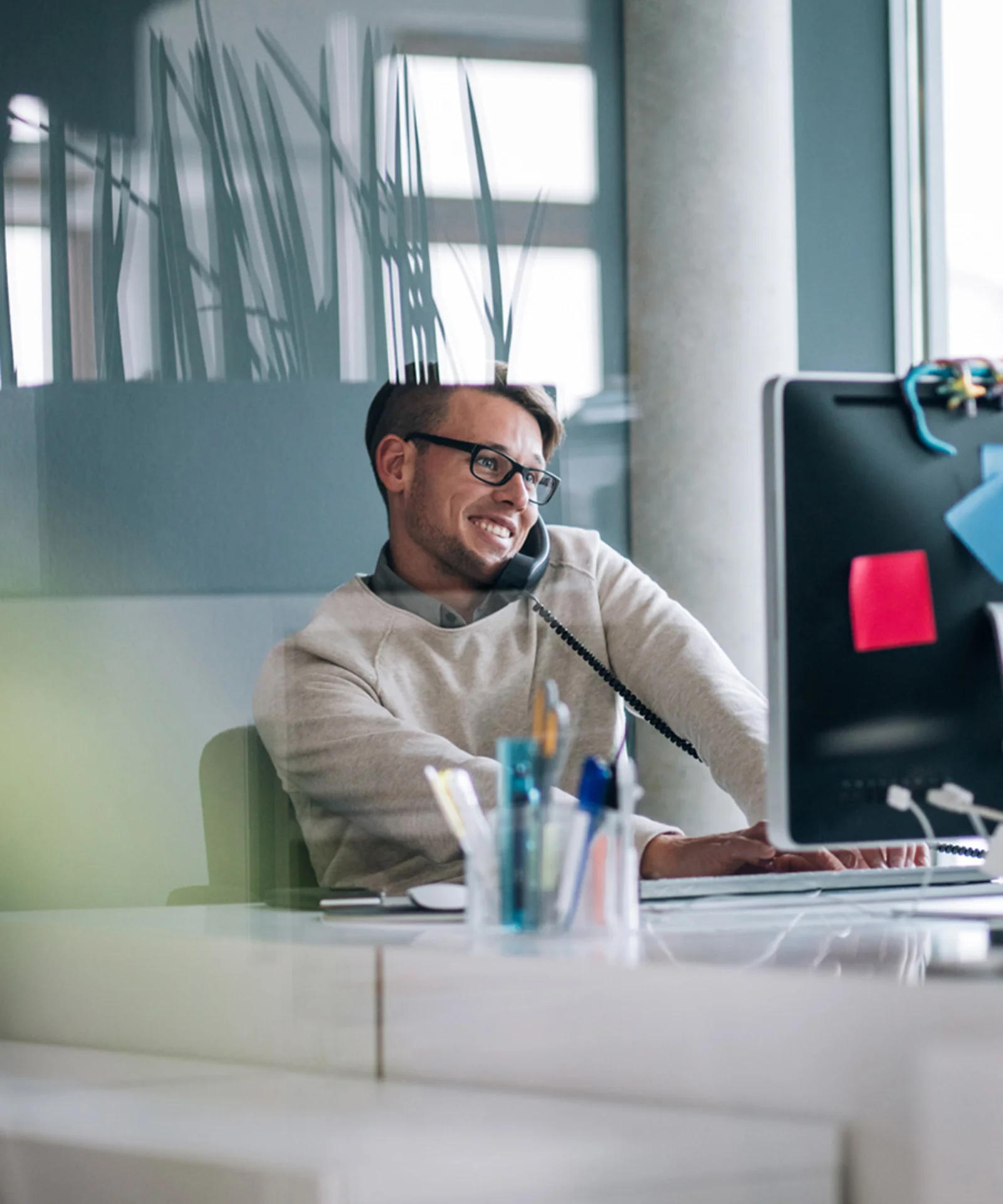 Smiling man on the phone working at a computer desk in a modern office.