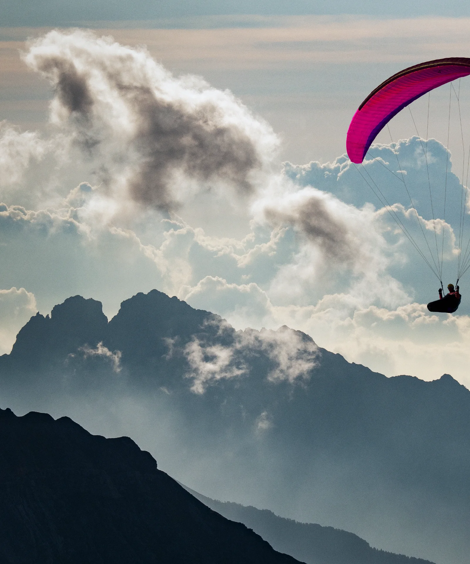 Gleitschirmflieger umgeben von Bergen und Wolken, verwendet als Key Visual für Cloud Services und Consulting.