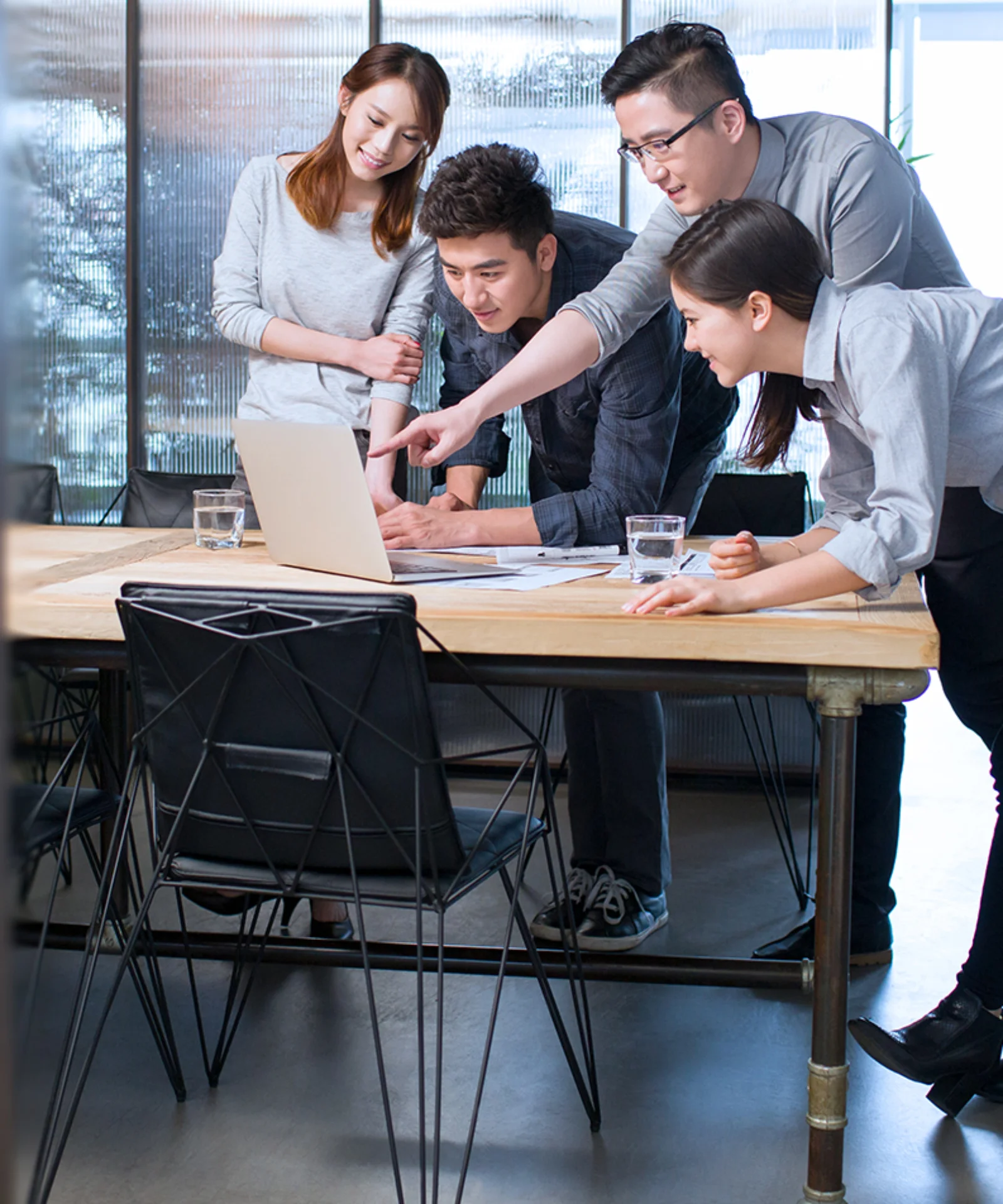 A group of four colleagues gathered around a laptop, engaged in a discussion, symbolizing teamwork, collaboration, and productivity in a contemporary workspace.