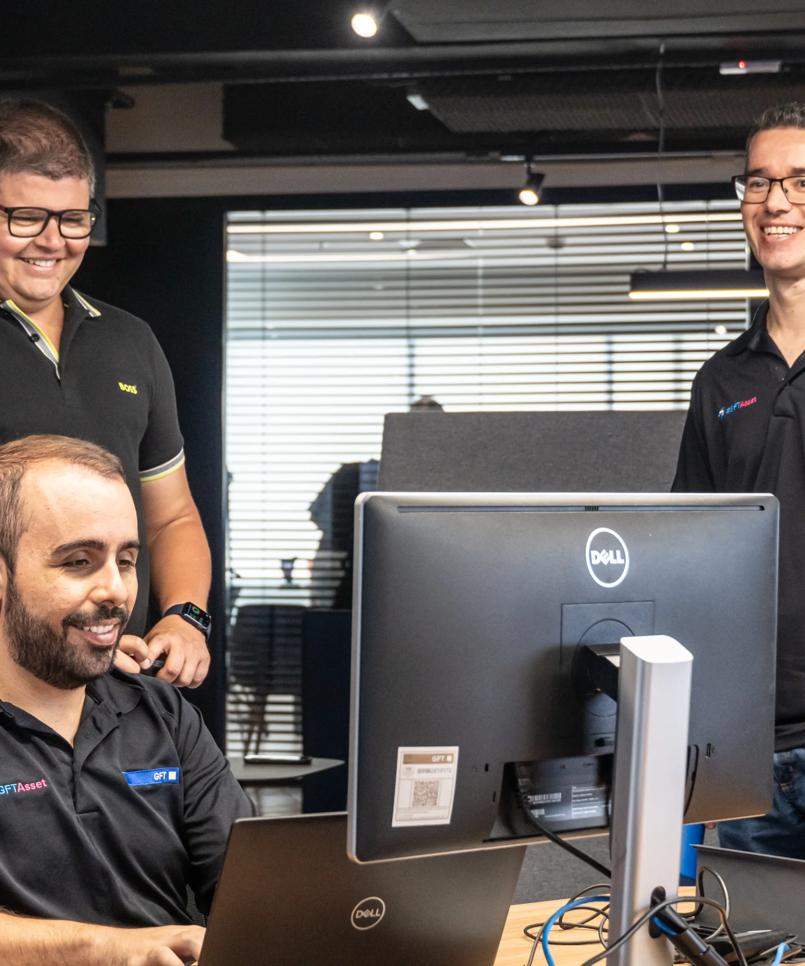 Three software developers collaborating and smiling while working together at a computer in a modern office environment.