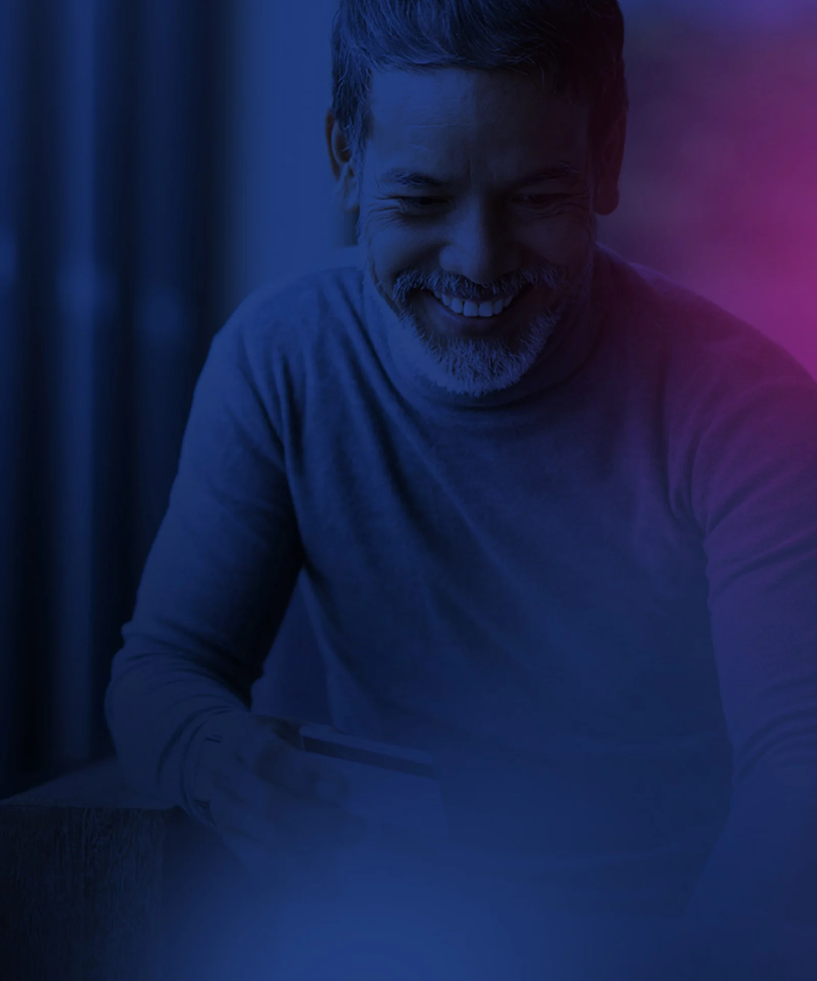 A man smiling while holding a credit card, making an online payment in a dimly lit, modern setting.