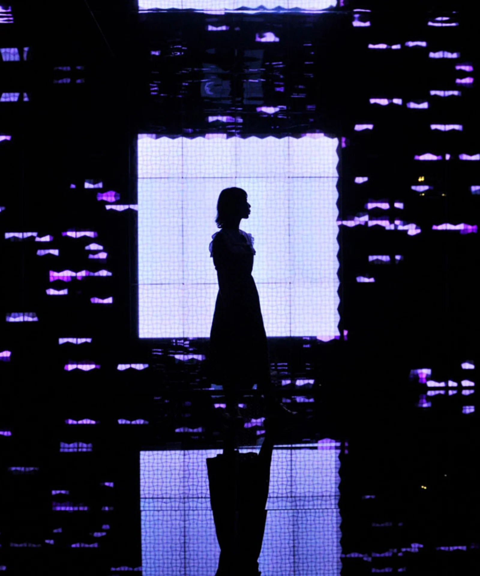 Silhouette of a woman standing in front of a bright screen, surrounded by digital patterns of purple light, symbolizing the intersection of technology and human presence.