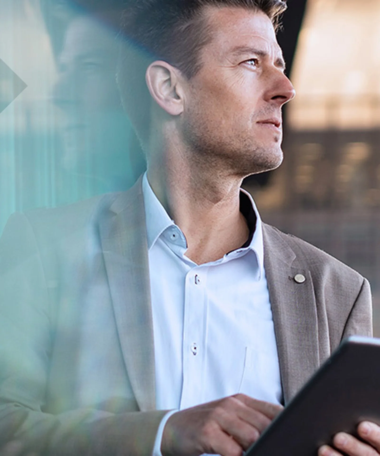 A business professional holding a tablet and looking thoughtfully out of a window, symbolizing strategic planning and modern technology in a corporate setting.