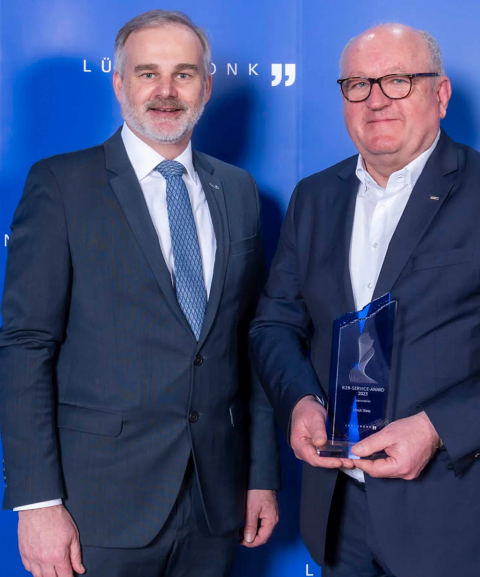 Ulrich Dietz and a colleague holding the Lünendonk B2B Service Award at an award ceremony, standing in front of a blue backdrop.