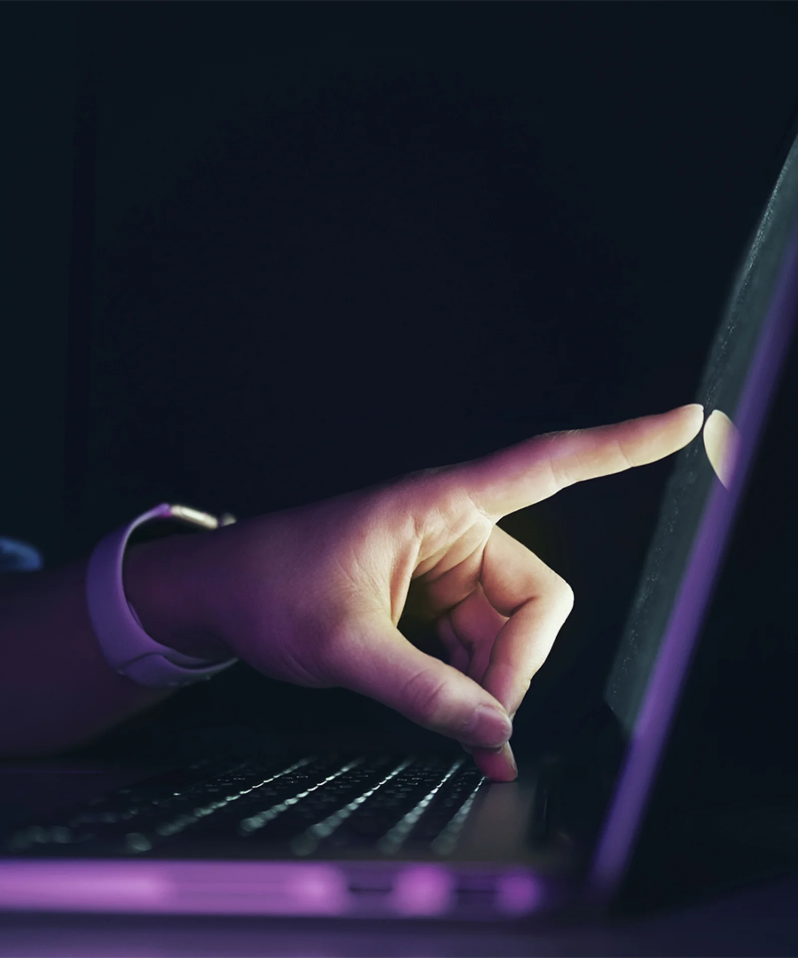 A close-up of a hand interacting with a laptop touchscreen in a dimly lit environment, representing seamless user experience and digital responsiveness.