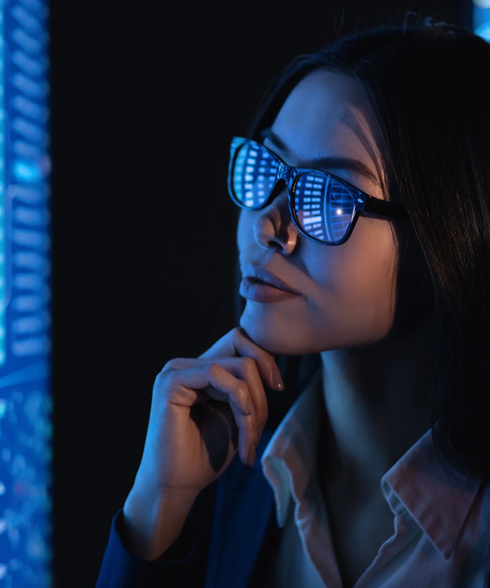 A woman in glasses, reflecting data charts, looks intently at multiple digital screens displaying various analytics and graphs.