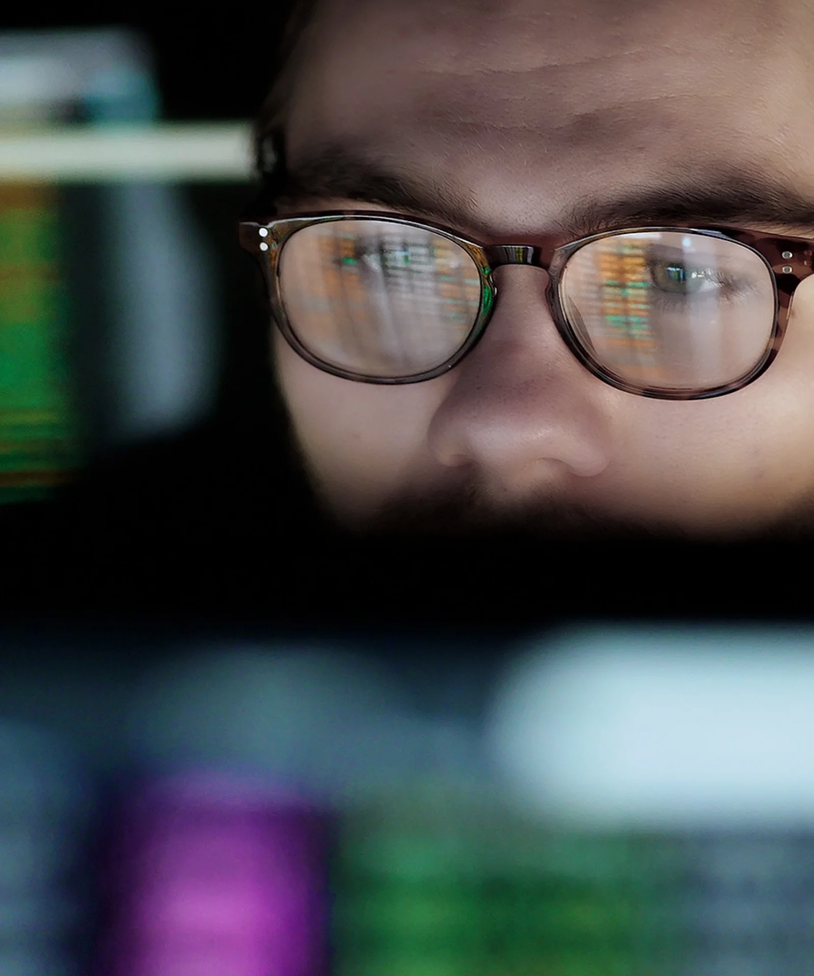 Close-up of a man wearing glasses, reflecting computer screens filled with data, representing the focus on machine learning operations (MLOps) in data-driven environments.