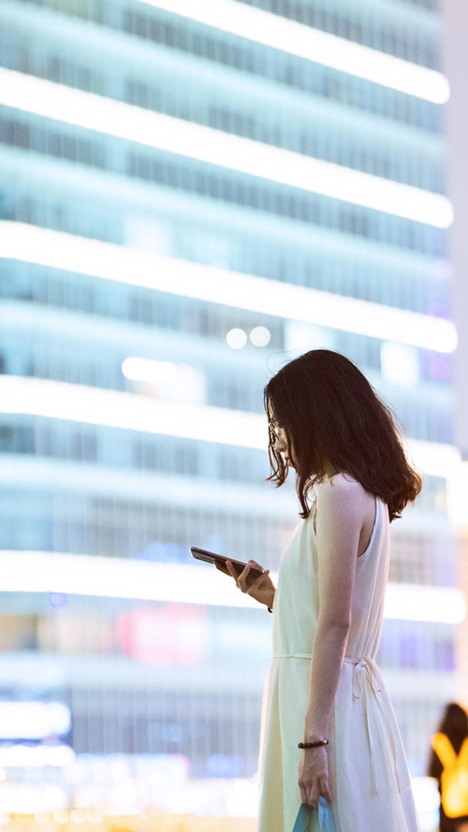 A professional woman using her smartphone with a modern cityscape in the background, symbolizing the impact of Central Bank Digital Currencies (CBDCs) on the future of commercial banking.