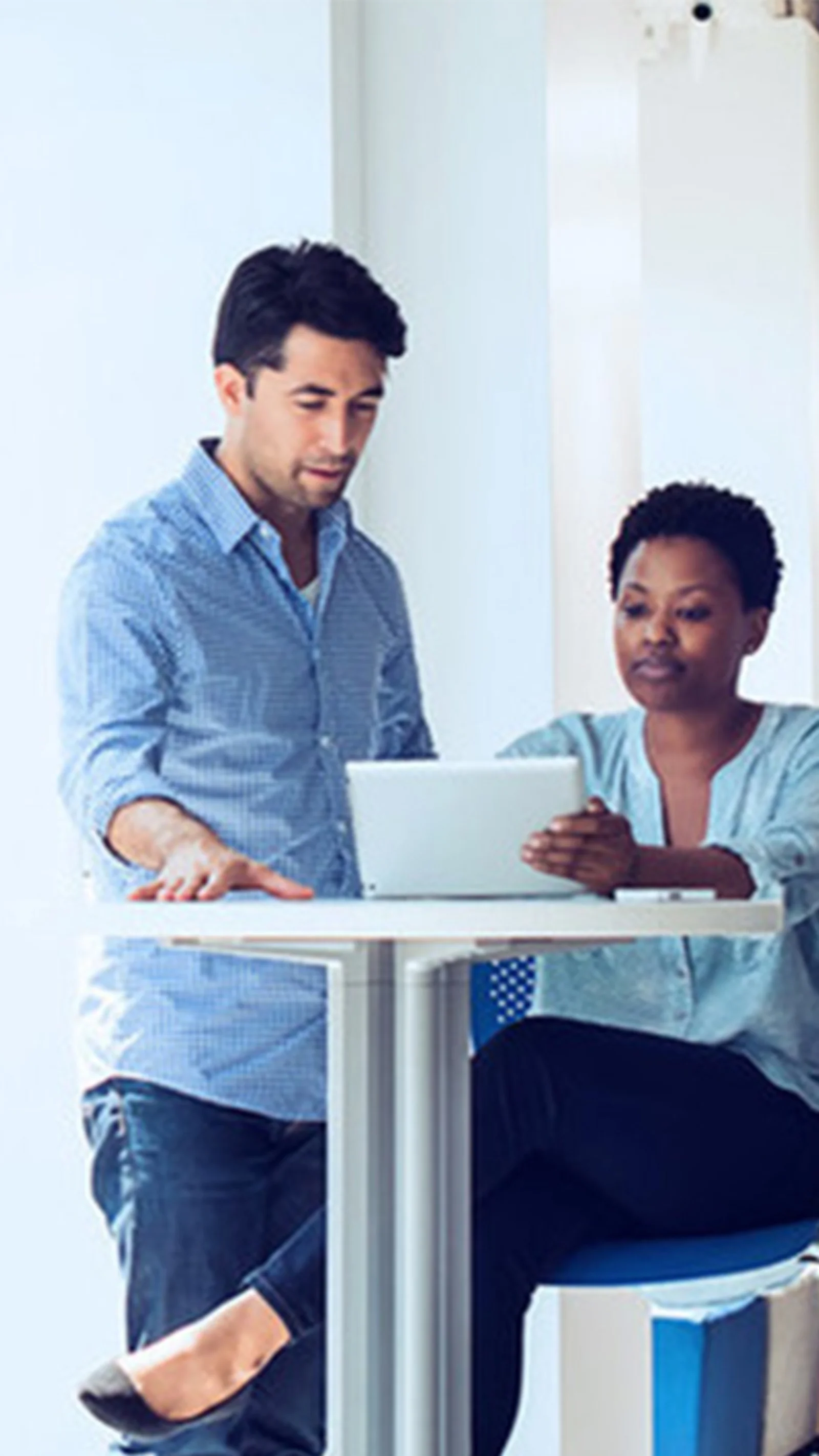 Two colleagues collaborating on a project while working on a laptop in a bright, modern office setting.