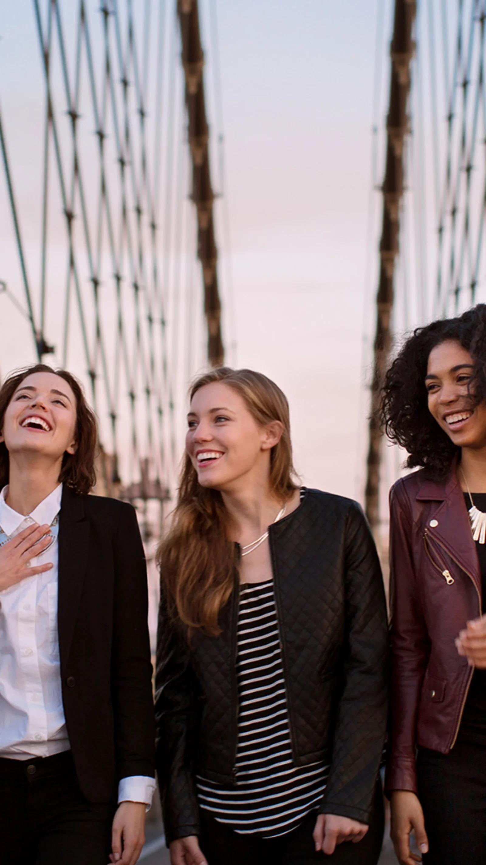 Três mulheres caminhando e rindo em uma ponte, simbolizando a entrega de conteúdo rápida, segura e contínua permitida pelo AWS CloudFront.