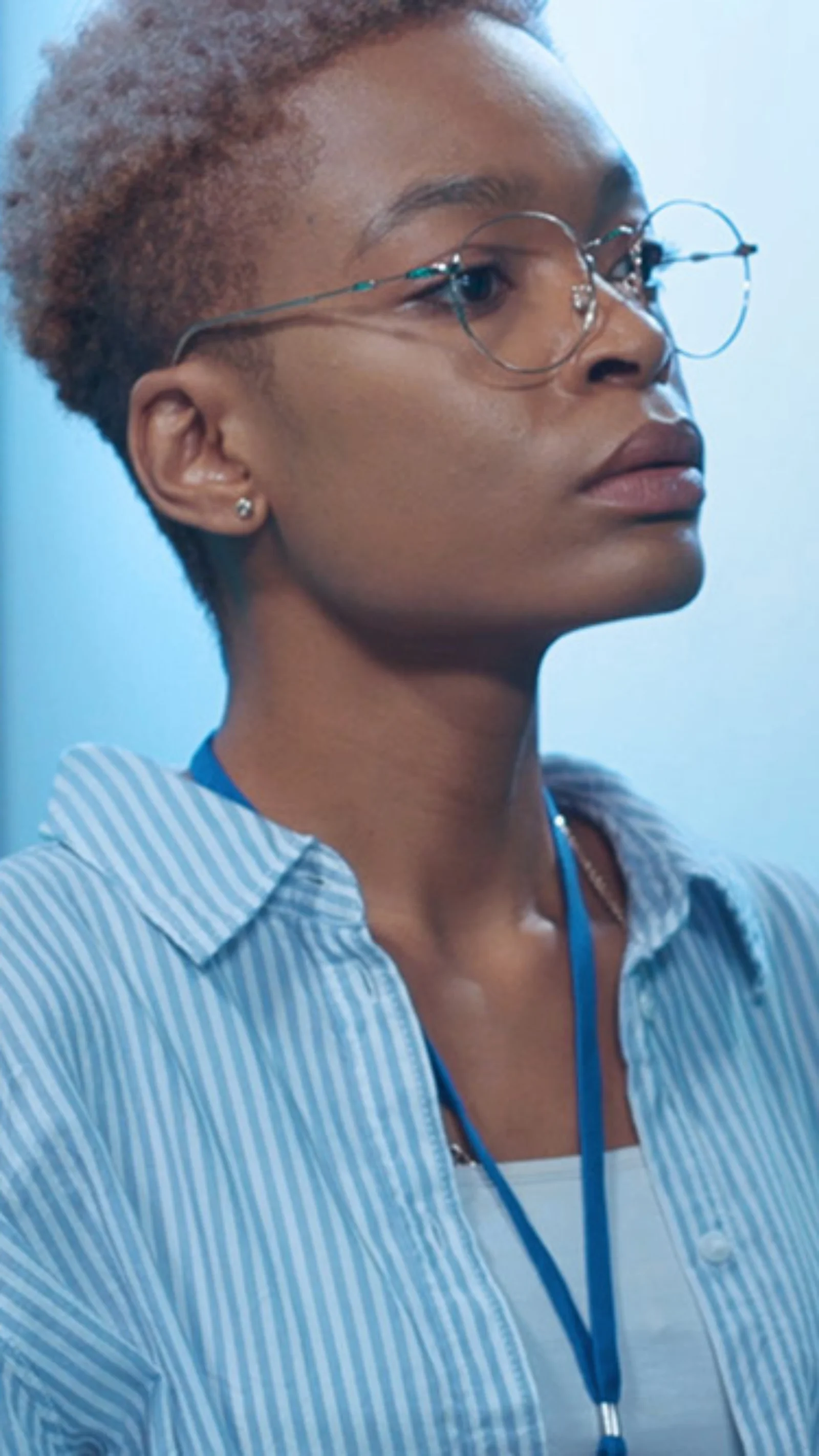 A focused tech professional with short hair and glasses analyzes data on a laptop in a blue-lit server room