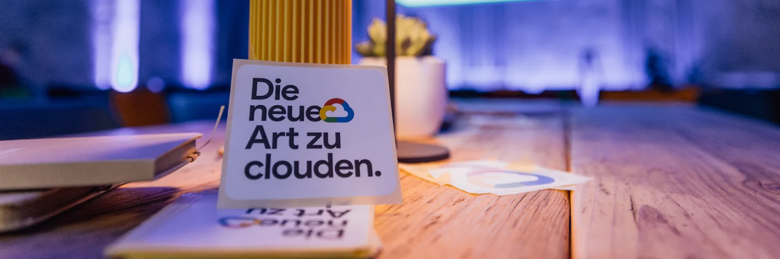 Nahaufnahme eines Tisches mit dem Schriftzug „Die neue Art zu clouden“ in einem atmosphärisch beleuchteten Raum auf dem Google Cloud Summit.