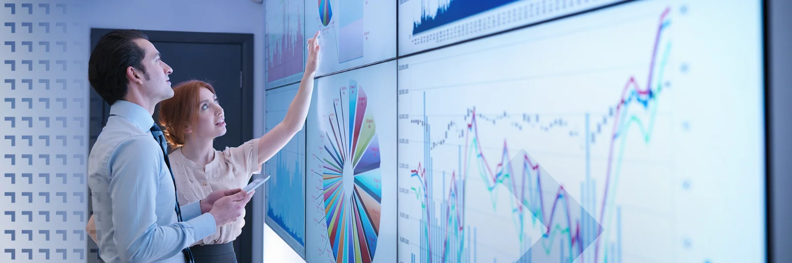 Two business analysts examining large digital screens displaying complex data visualizations, graphs, and charts, focused on analyzing trends.