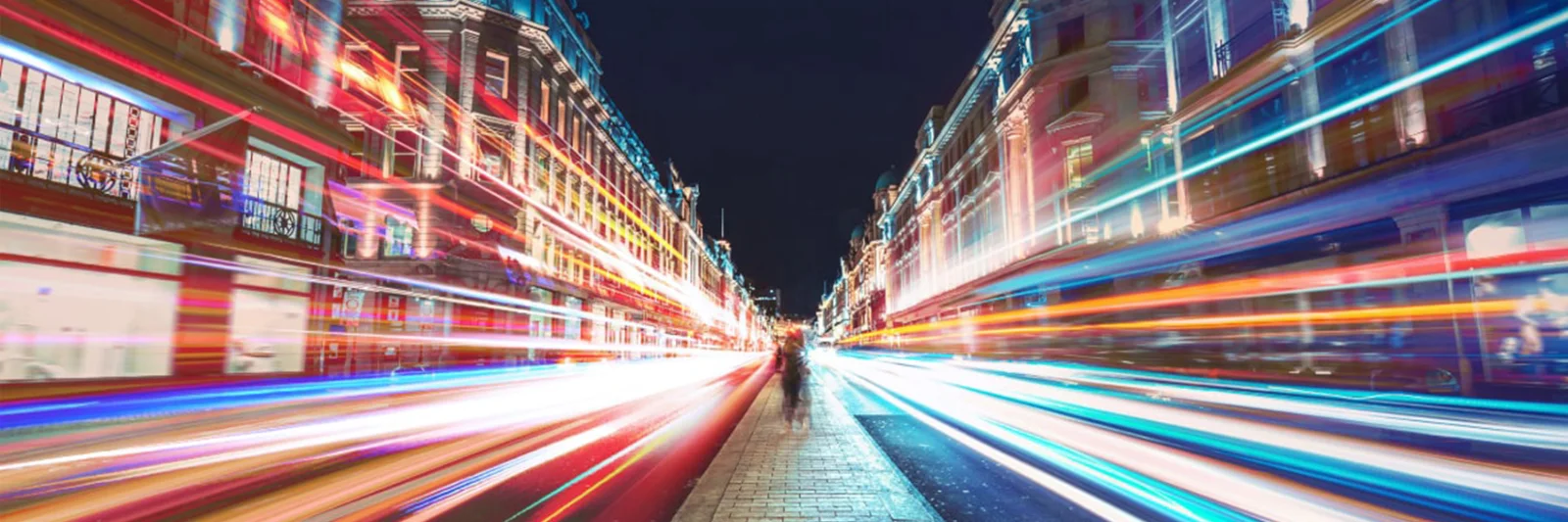 A vibrant city street at night, illuminated by streaks of colorful lights, representing the fast-paced and dynamic nature of modern banking and finance.