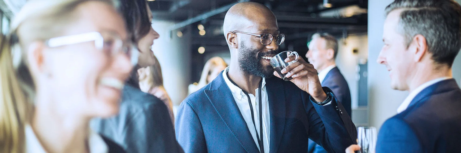 Professionals engaging in conversation and networking at a GFT event, with one man drinking coffee and others smiling and talking.