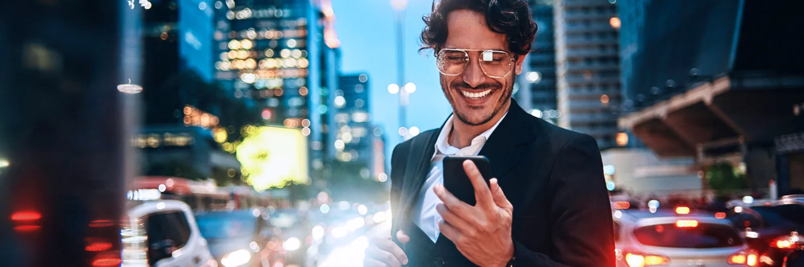 A smiling business professional interacts with a smartphone in a bustling city at night, symbolising the future of digital banking.