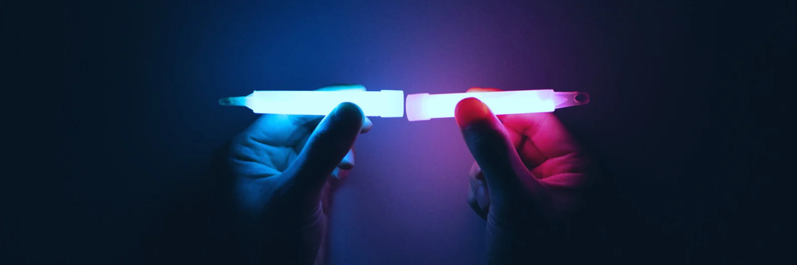 Two hands holding glowing light sticks, one blue and one pink, symbolizing the fusion and connection in platform modernisation.