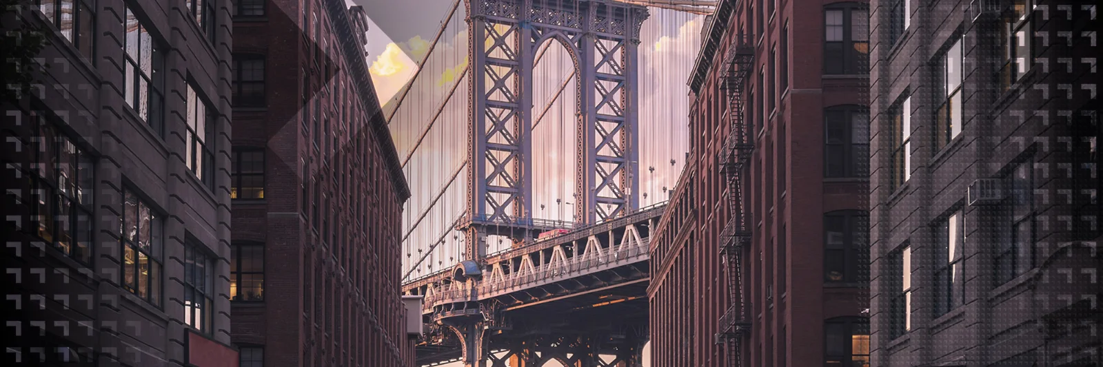 A view of the Manhattan Bridge framed by tall urban buildings at sunset, showcasing the architectural beauty and urban landscape of New York City.