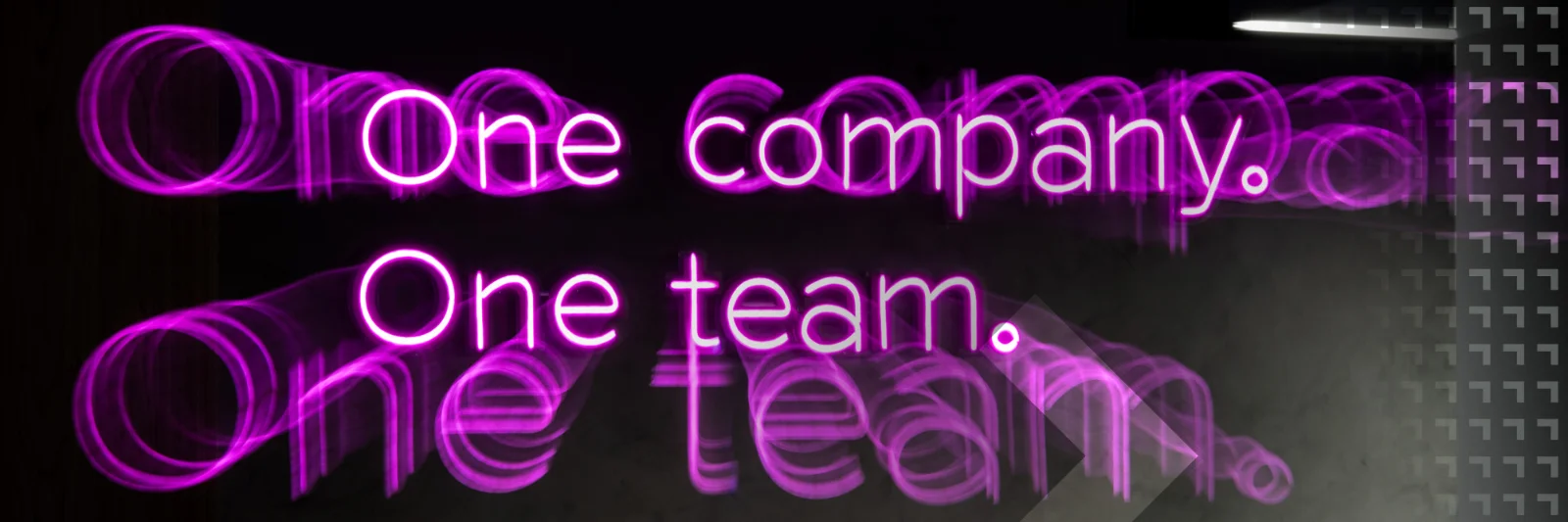 Neon sign with the words &quot;One company. One team.&quot; in vibrant pink, emphasizing unity and collaboration within an organization.