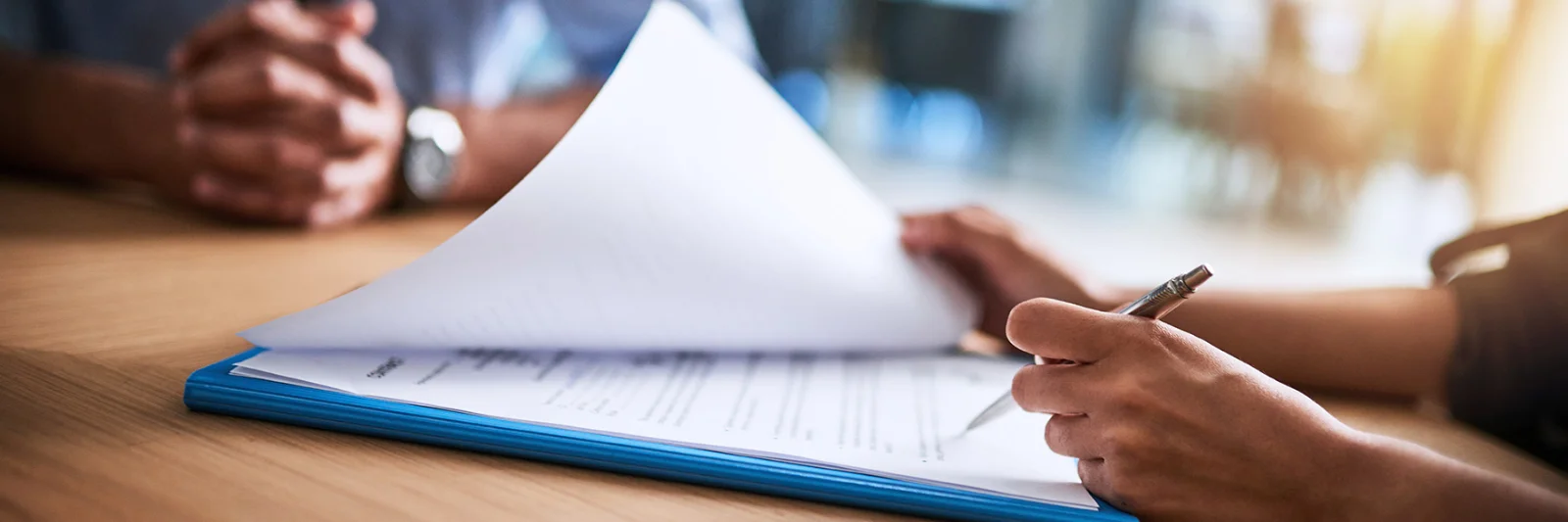 Close-up of hands reviewing a document with a pen, symbolising professional collaboration and careful consideration in decision-making.