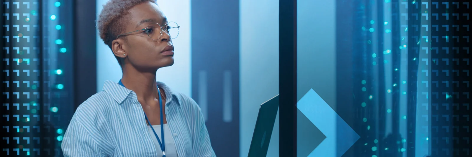 A focused tech professional with short hair and glasses analyzes data on a laptop in a blue-lit server room