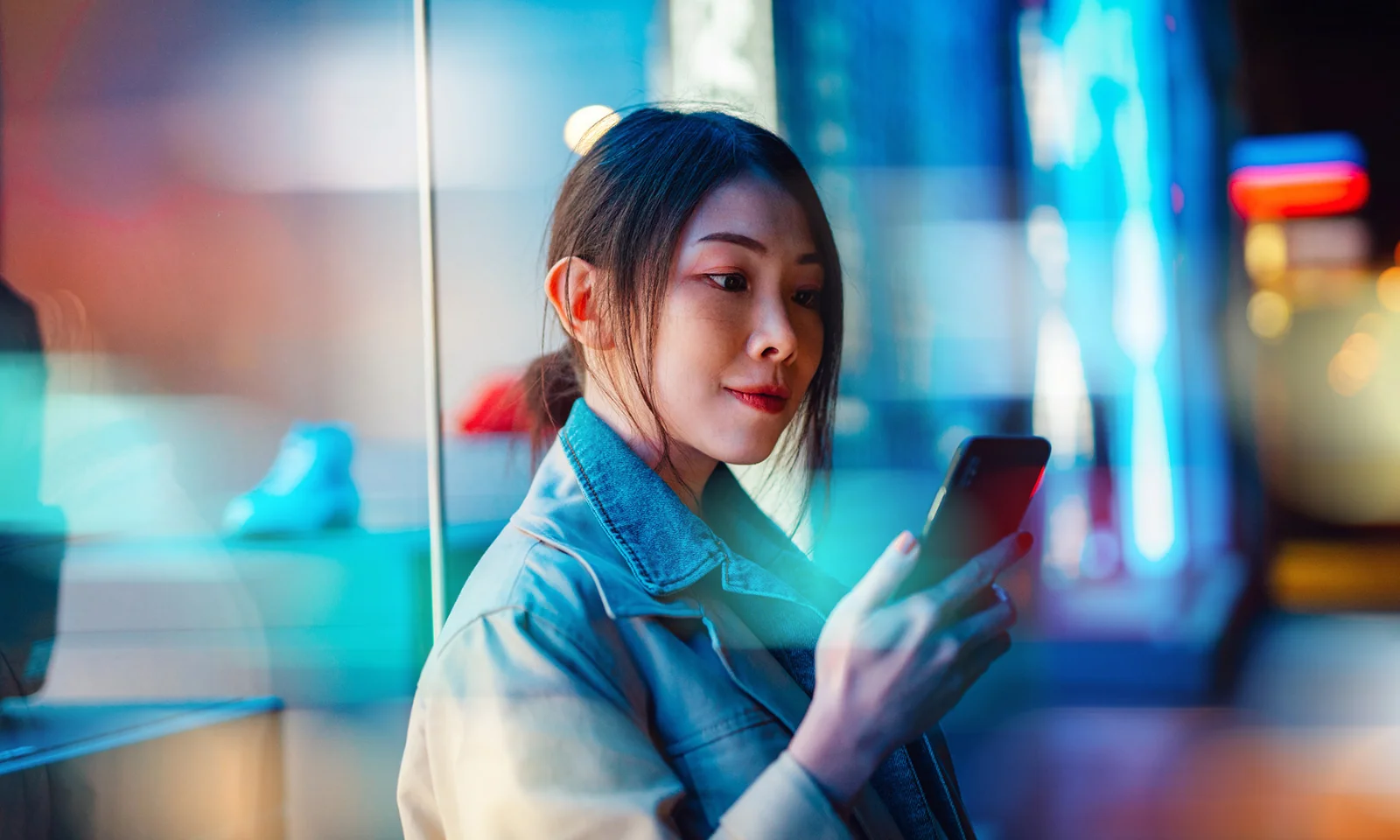 A young woman interacts with her smartphone while standing in a vibrant, neon-lit urban environment at night.