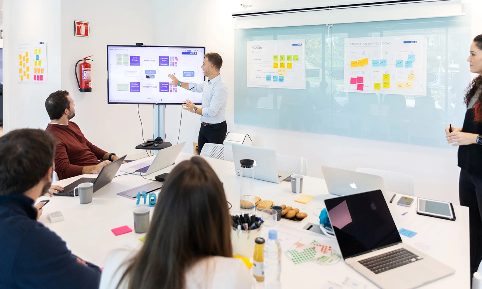 A group of professionals engaged in a design services experience transformation workshop, with one person presenting on a digital screen while others participate with laptops and notes.