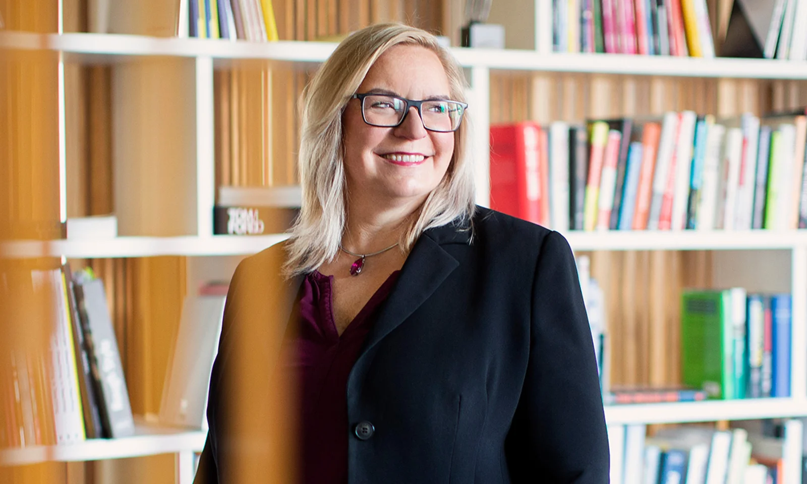 Marika Lulay, a member of the GFT Administrative Board, smiling while standing in front of a bookshelf, wearing a black blazer and glasses, representing thought leadership in the technology sector.