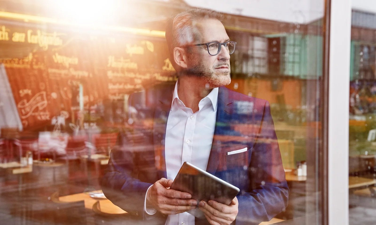 Business professional holding a tablet and looking through a cafe window, representing GFT&#039;s focus on digital transformation and strategic innovation.