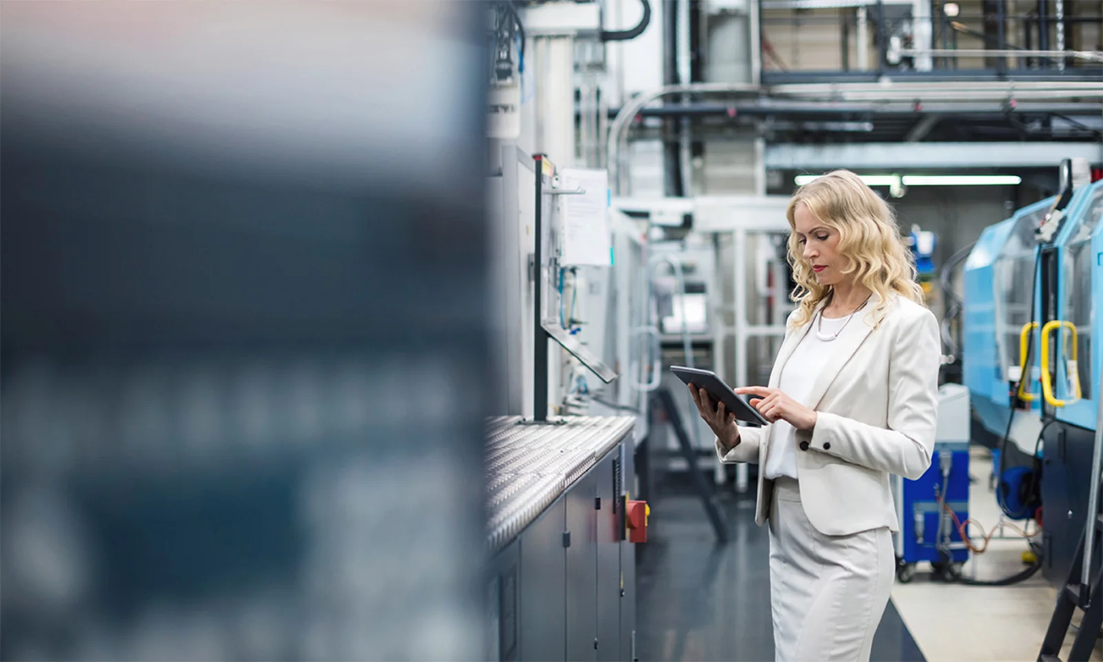 A professional woman in a light-coloured suit using a tablet in an advanced manufacturing facility, symbolising sustainable production practices in a smart factory environment.