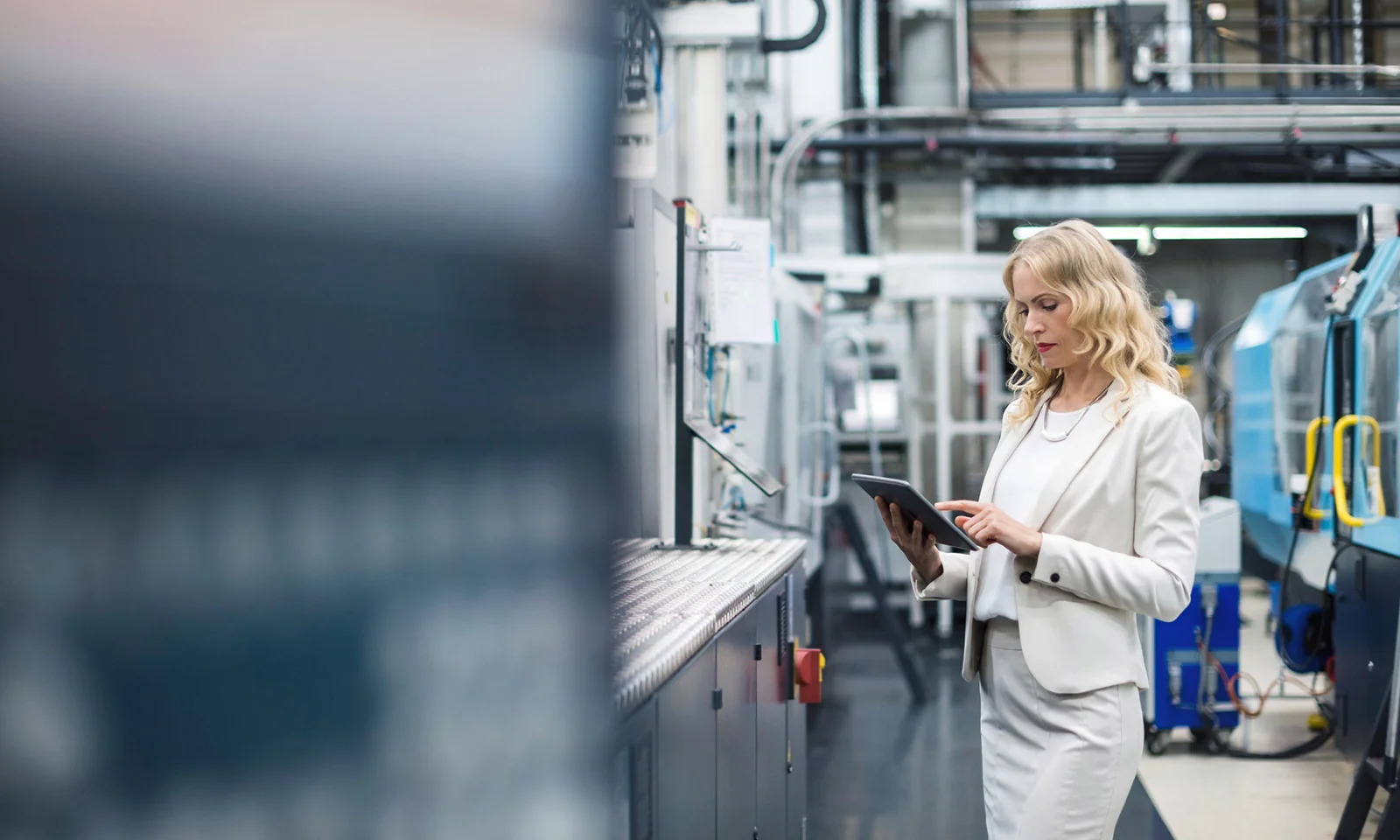 Businesswoman in a white suit using a tablet while inspecting a manufacturing facility.