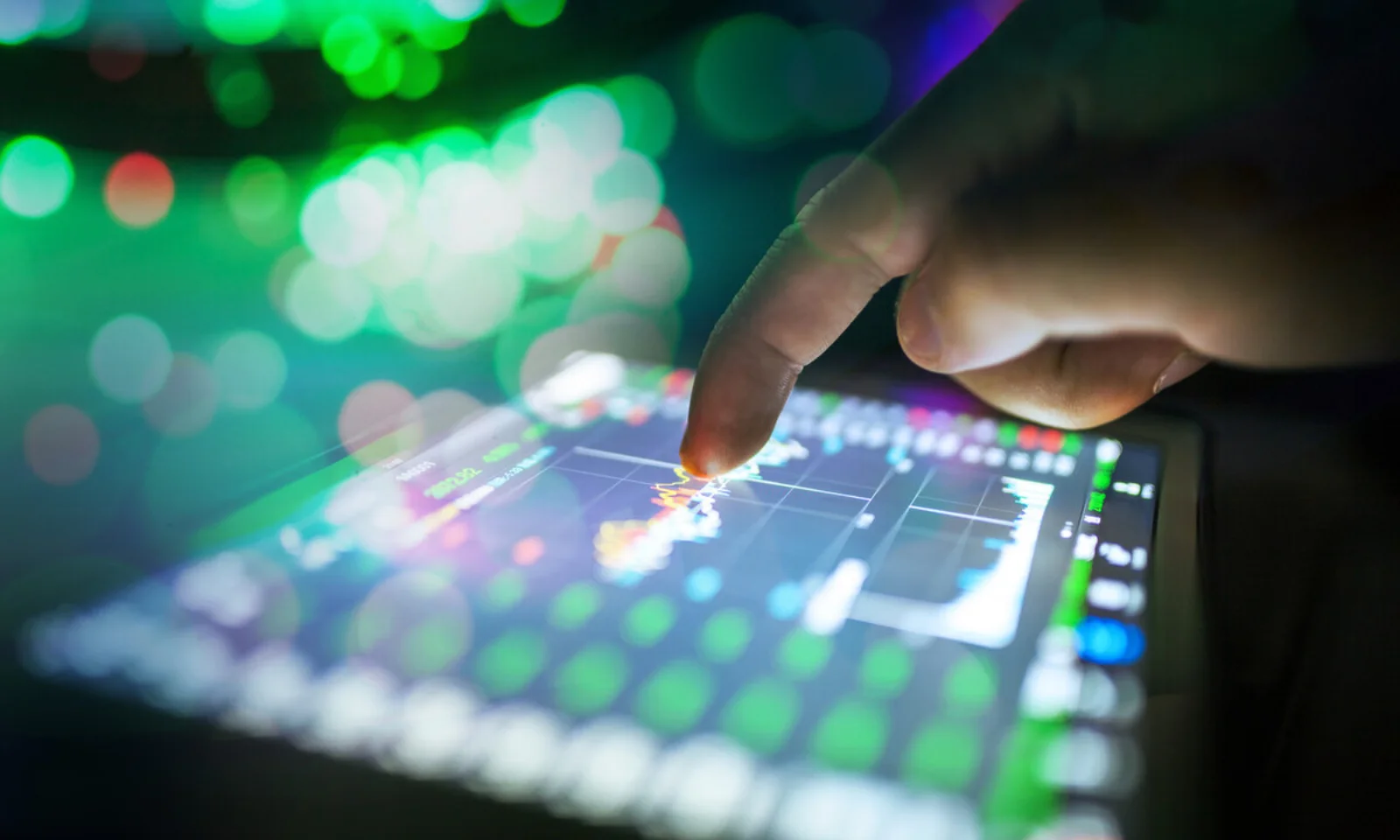 Close-up of a hand interacting with a touchscreen device displaying data charts, representing real-time data analysis and technology.