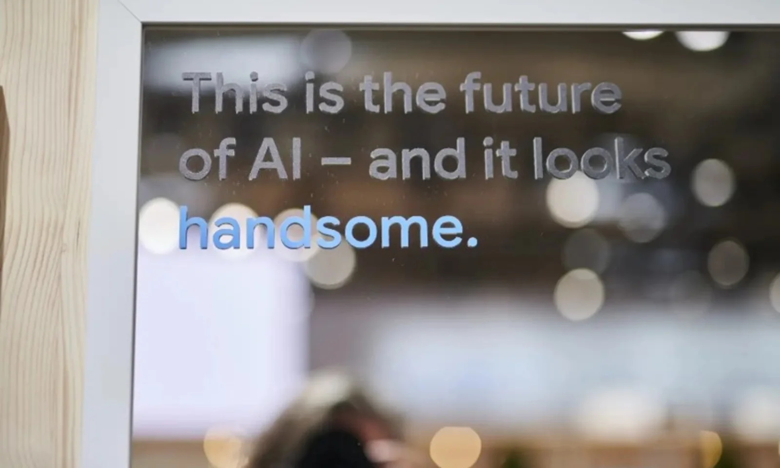 Ein Zitat auf einer spiegelnden Oberfläche von der Hannover Messe, das lautet: „This is the future of AI – and it looks handsome.“ Der Hintergrund zeigt verschwommene Lichter, die eine Messe-Atmosphäre andeuten.