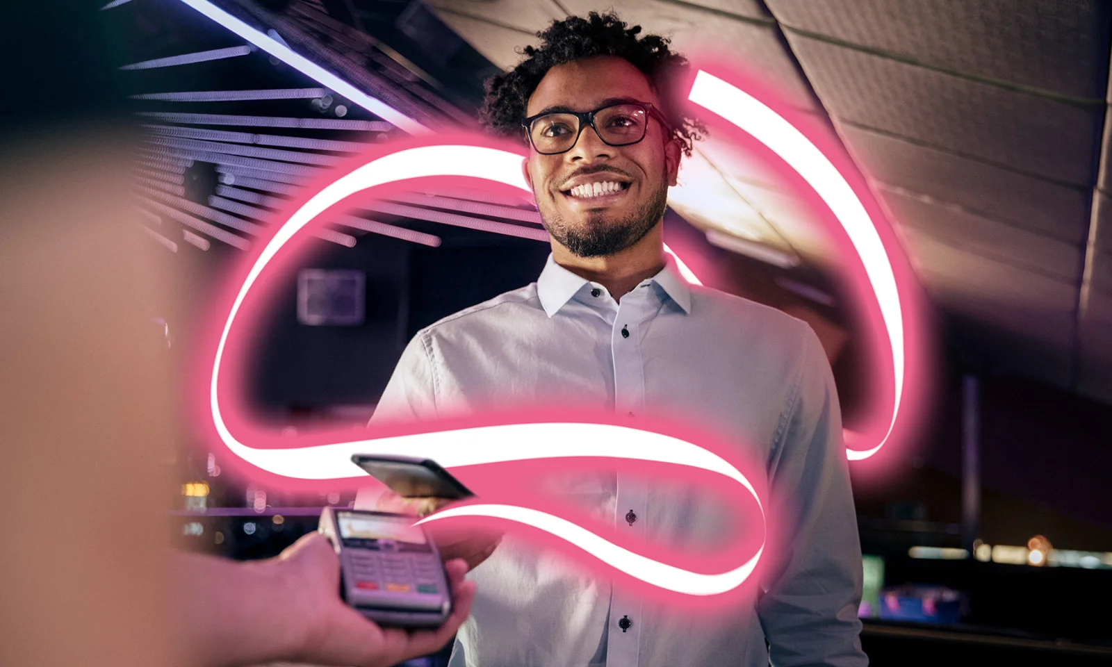 Hombre sonriendo mientras realiza un pago sin contacto con un teléfono inteligente, rodeado de una luz rosa brillante.