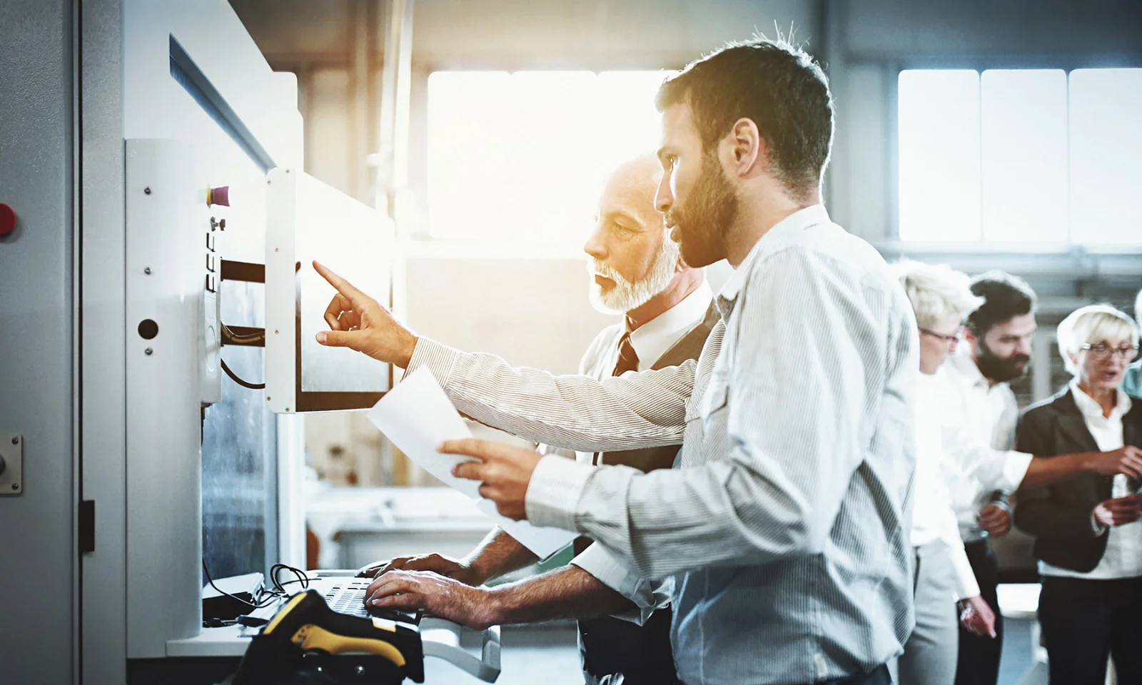 Two technicians operating a piece of industrial machinery while discussing settings in a manufacturing facility.