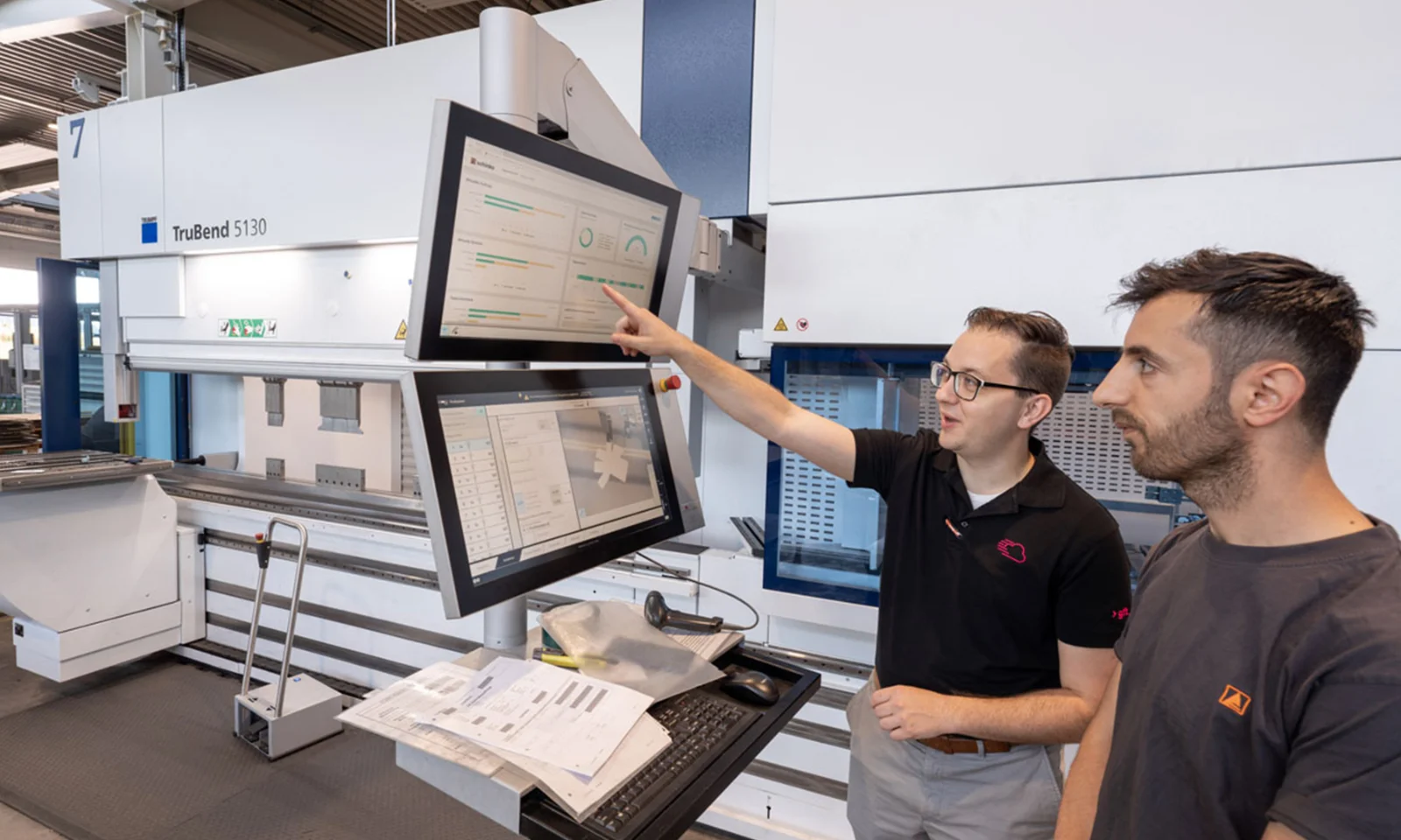 Two professionals collaborate in front of a TruBend 5130 machine, discussing data displayed on dual screens, representing transparent shopfloor management.