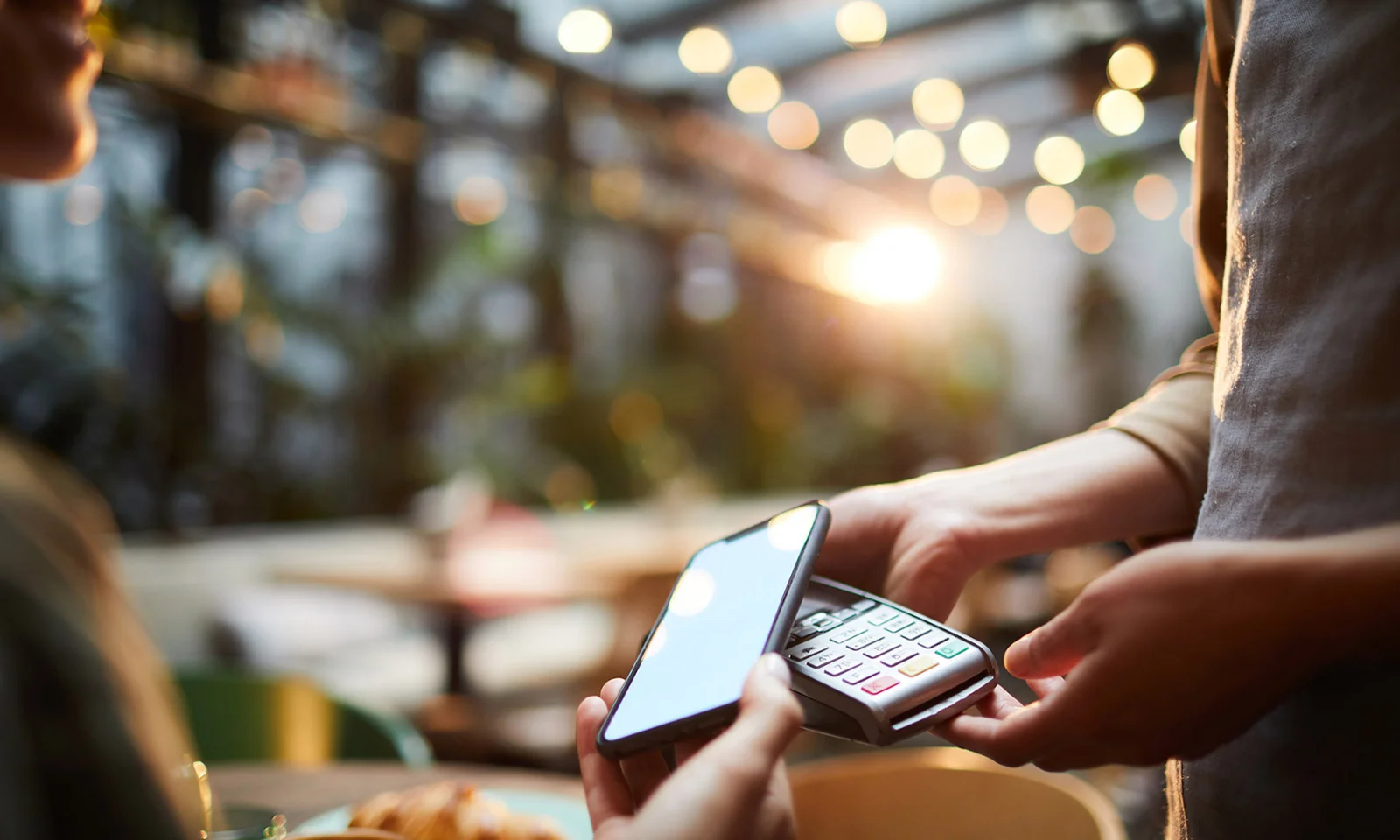 Close-up of a person making a mobile payment with a smartphone in a modern cafe, highlighting GFT&#039;s digital payment solutions