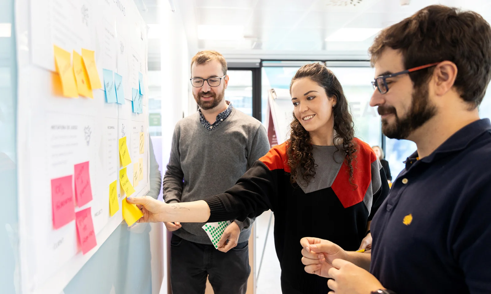 Three professionals collaborating during a design services experience transformation workshop, using sticky notes on a board to brainstorm and organize ideas.