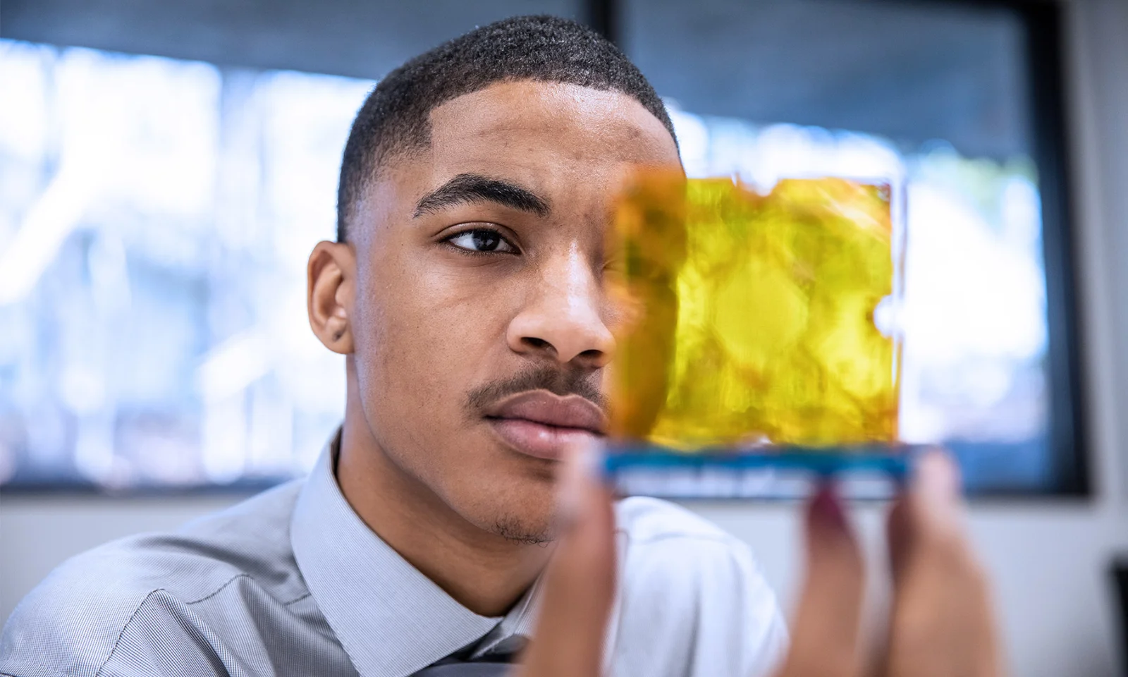 A focused professional examining a transparent yellow component, symbolising precision and attention to detail in a modern workspace.