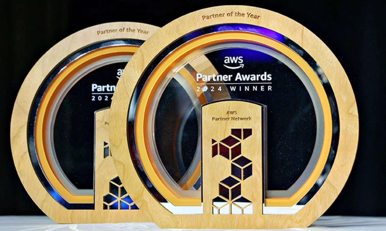 Close-up of two AWS Partner Awards 2024 trophies, labeled &quot;Partner of the Year,&quot; featuring the AWS Partner Network logo and elegant wood-and-glass design.