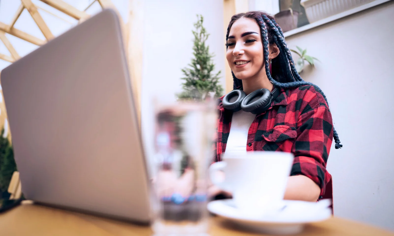 Young woman with braided hair and headphones around her neck working on a laptop at an outdoor cafe.