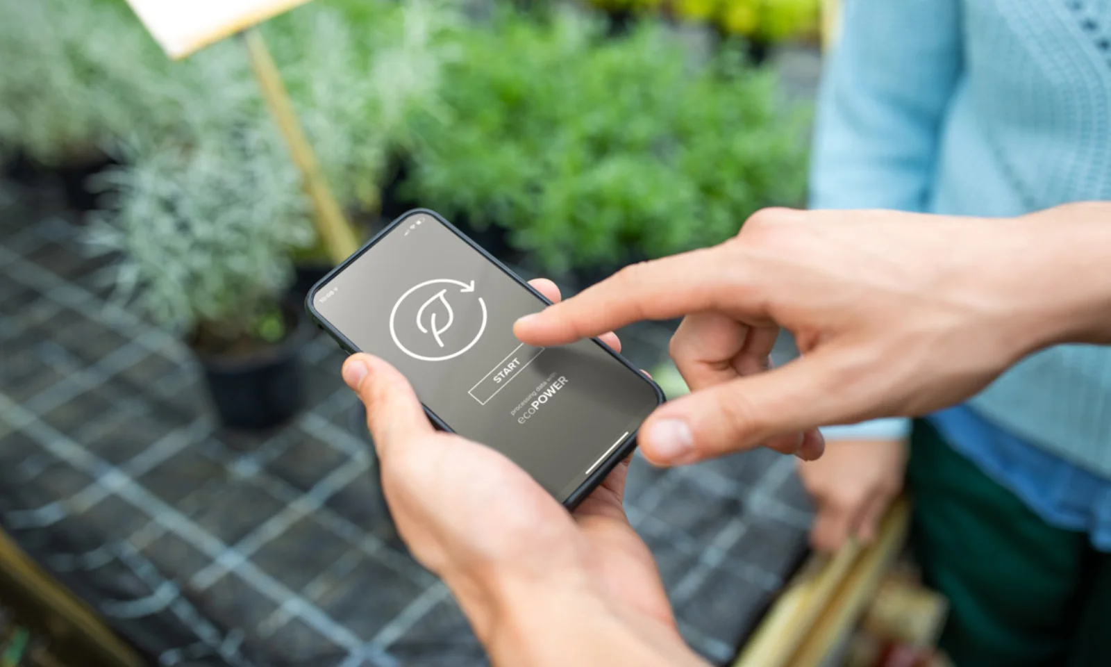 Close-up of hands using a mobile app focused on sustainable agriculture, with plants visible in the background.