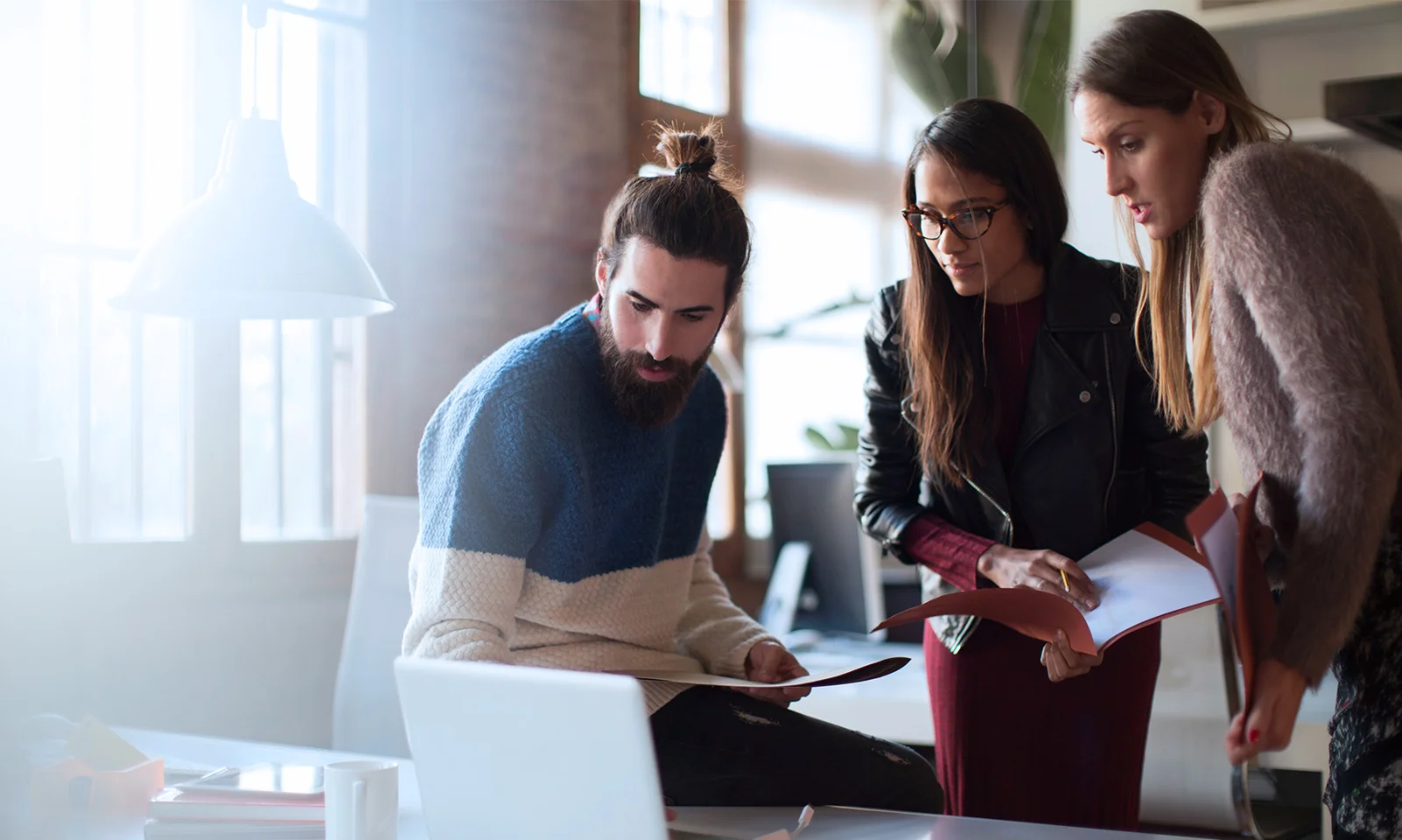 Three professionals collaborating around a laptop, symbolising the partnership between GFT and 10x Banking to drive innovation in the financial services sector.